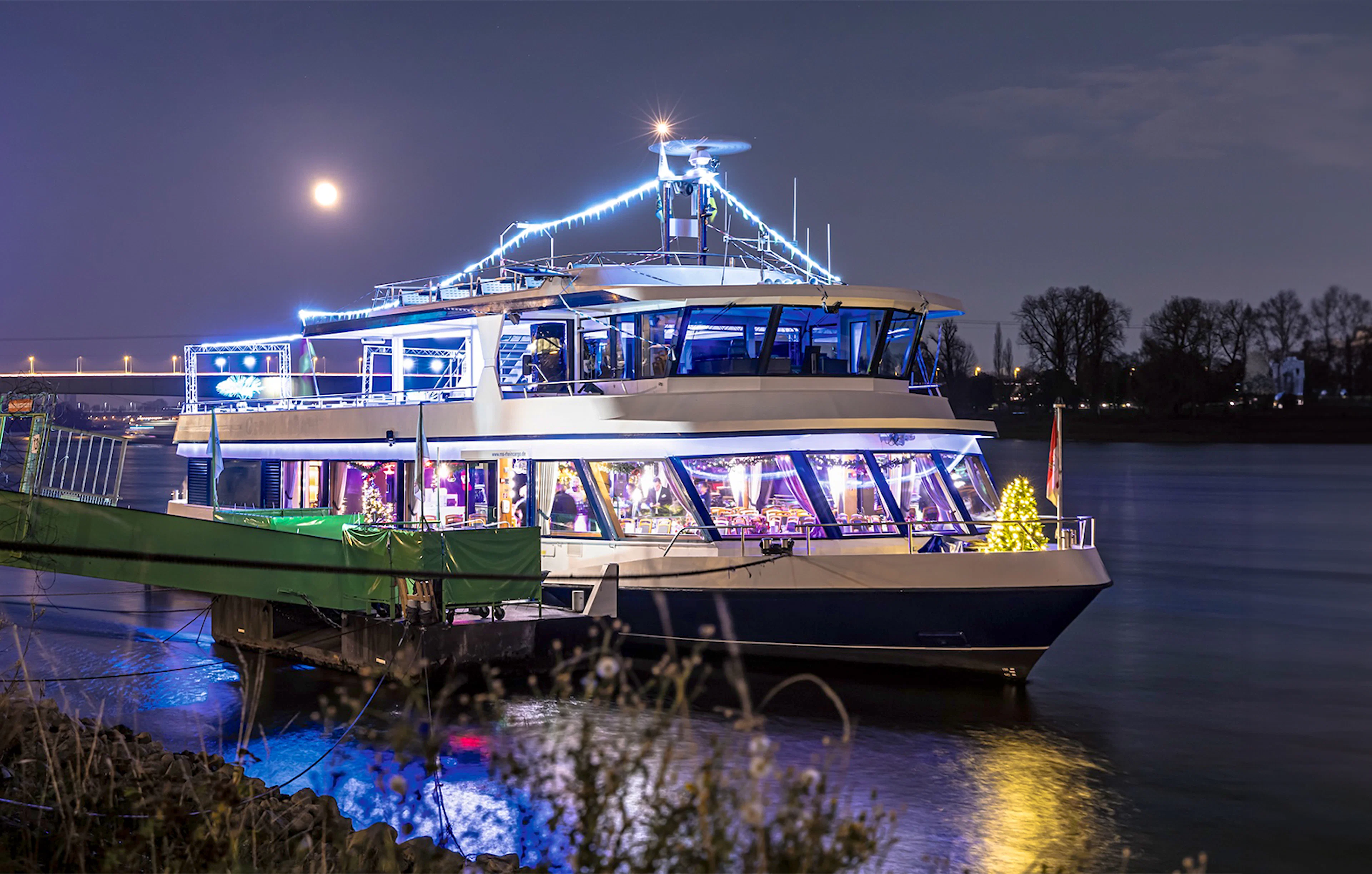 Festively lit boat on the Rhine River during Cologne Advent tour with moonlit sky.