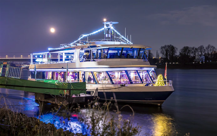 Festively lit boat on the Rhine River during Cologne Advent tour with moonlit sky.