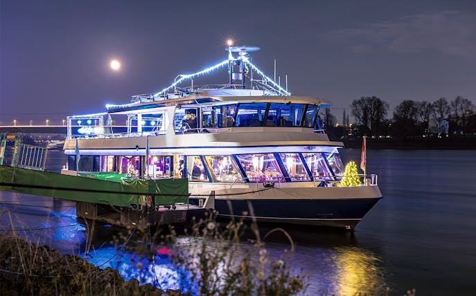 Festively lit boat on the Rhine River during Cologne Advent tour with moonlit sky.
