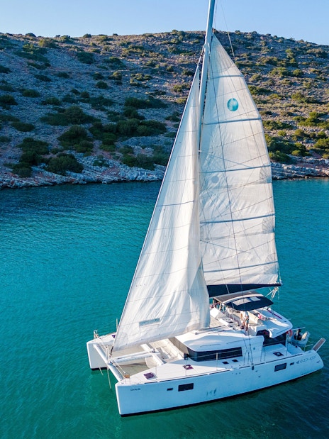 Catamaran sailing near Spinalonga, Crete, with rocky coastline in the background.
