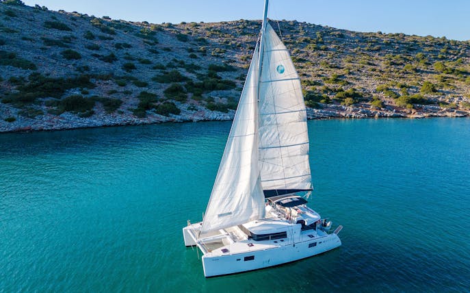Catamaran sailing near Spinalonga, Crete, with rocky coastline in the background.