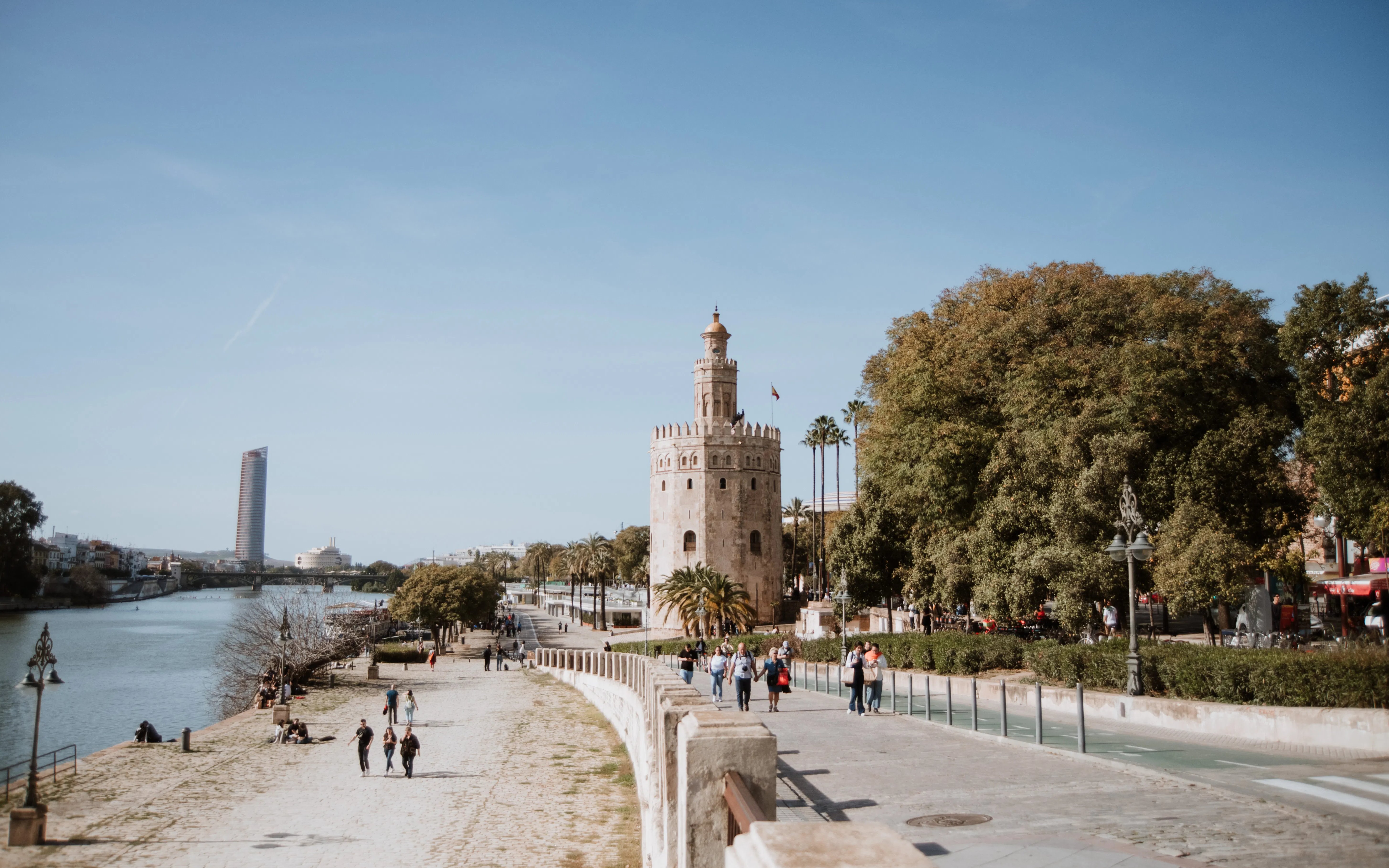 Torre del Oro by the Guadalquivir River in Seville, Spain, with people walking nearby.