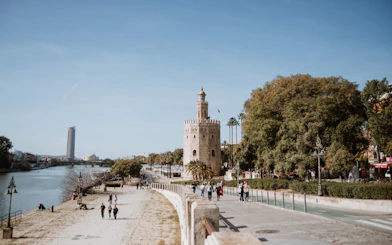 Torre del Oro by the Guadalquivir River in Seville, Spain, with people walking nearby.