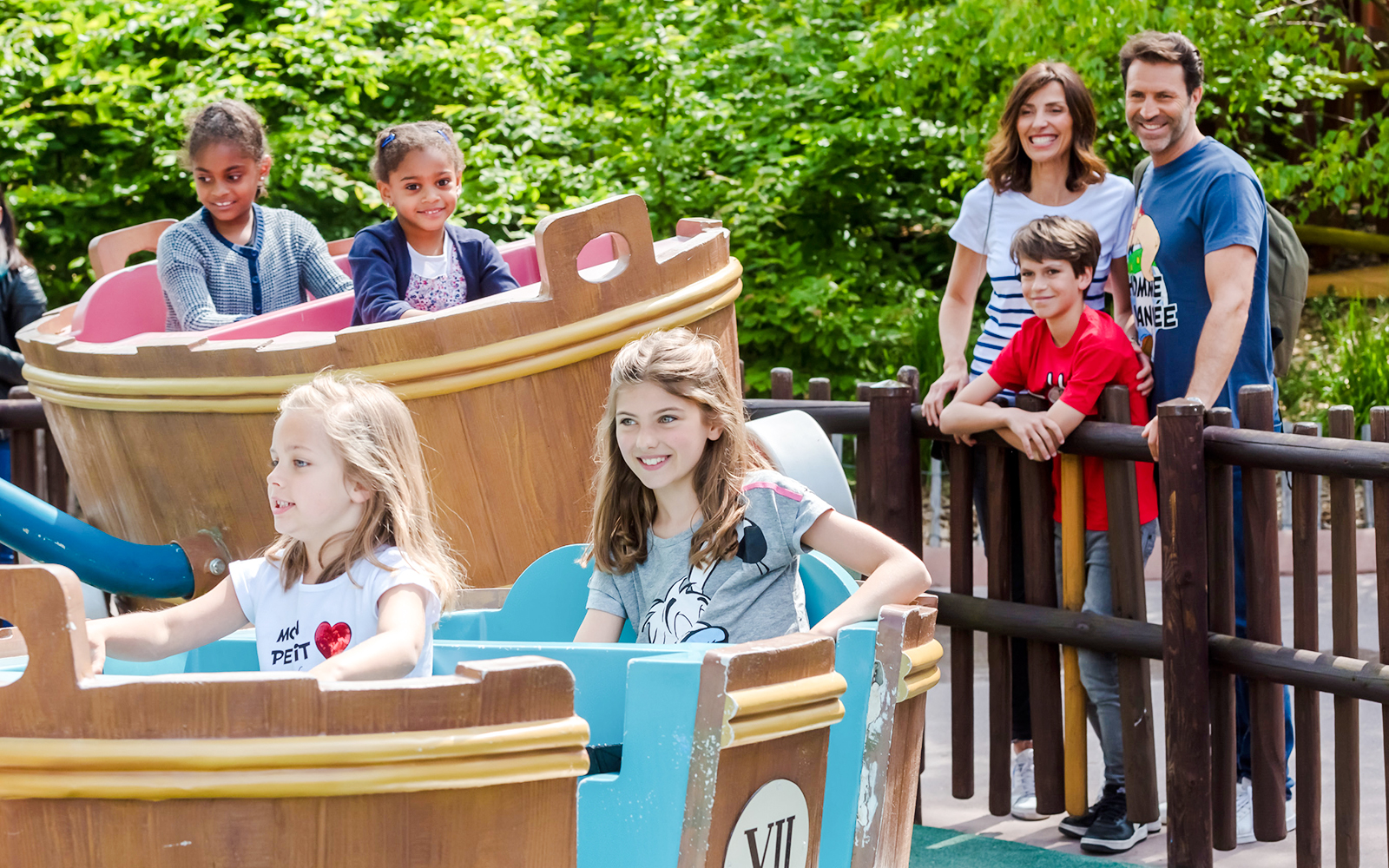Children enjoying a boat ride at Parc Astérix with family watching nearby.
