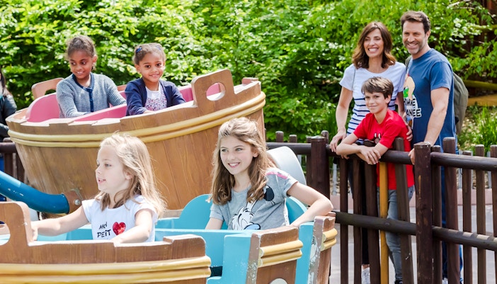 Children enjoying a boat ride at Parc Astérix with family watching nearby.