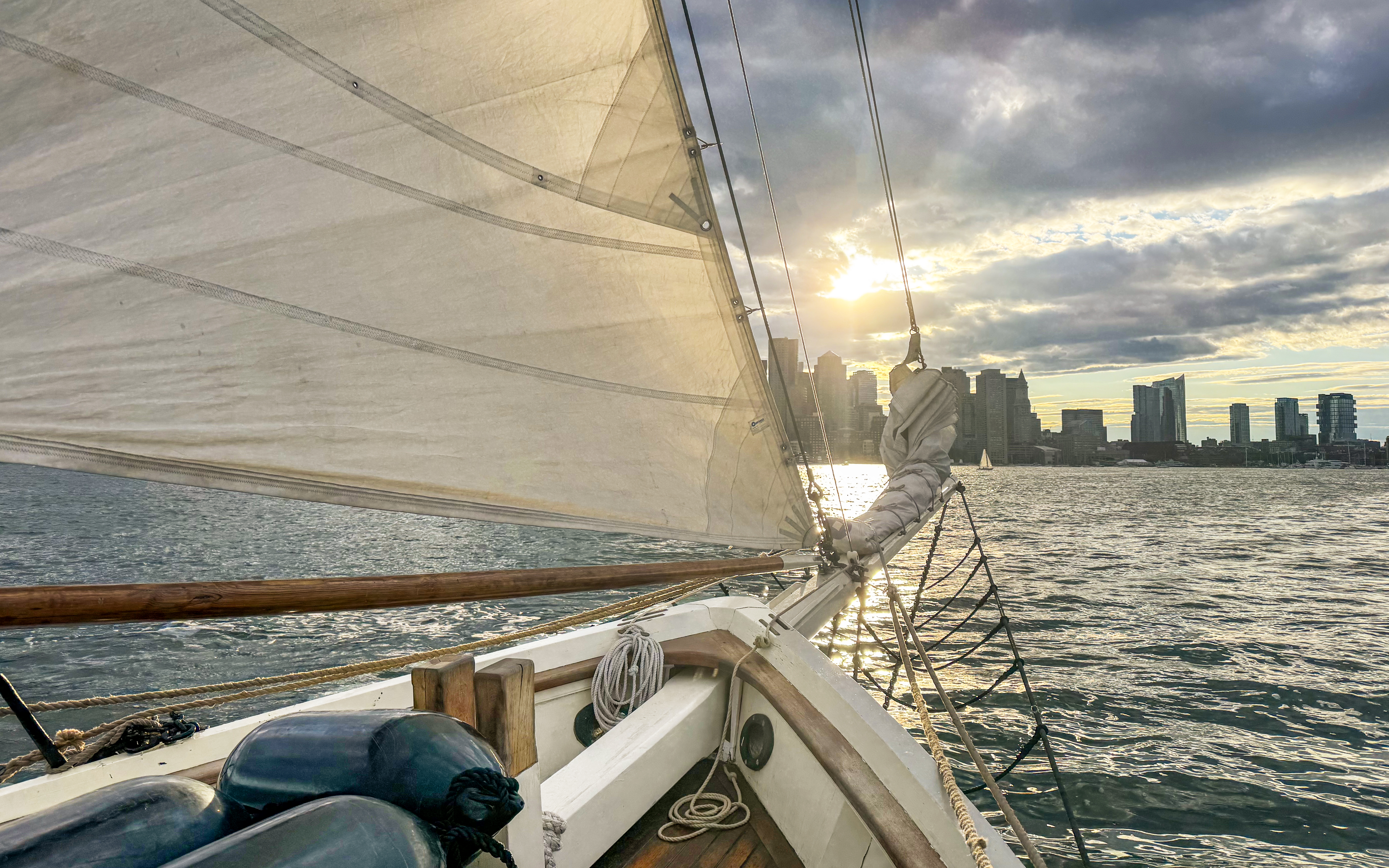 Sailing on Liberty Fleet of Tall Ships with Boston skyline at sunset.