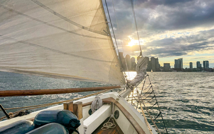Sailing on Liberty Fleet of Tall Ships with Boston skyline at sunset.