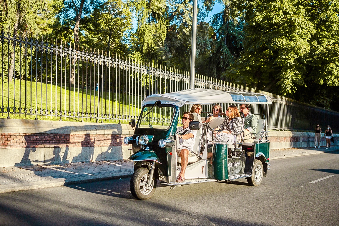 Eco Tuk Tuk tour with passengers driving past a park in a sunny city.