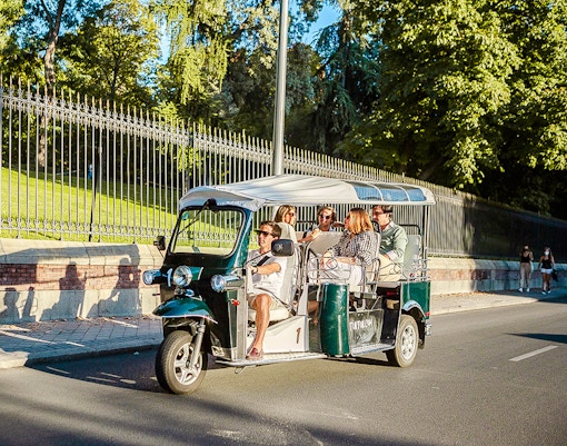 Eco Tuk Tuk tour with passengers driving past a park in a sunny city.