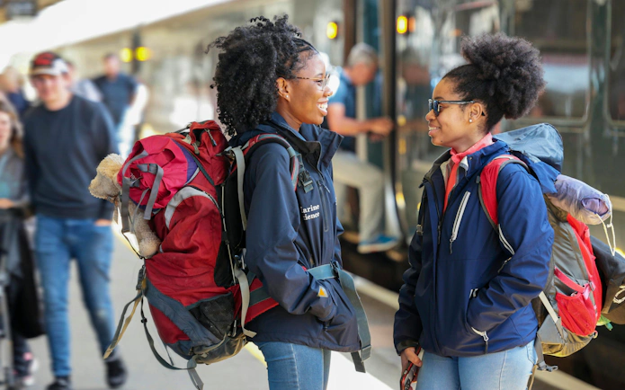 Travelers with backpacks at a UK train station platform, BritRail Consecutive Pass.