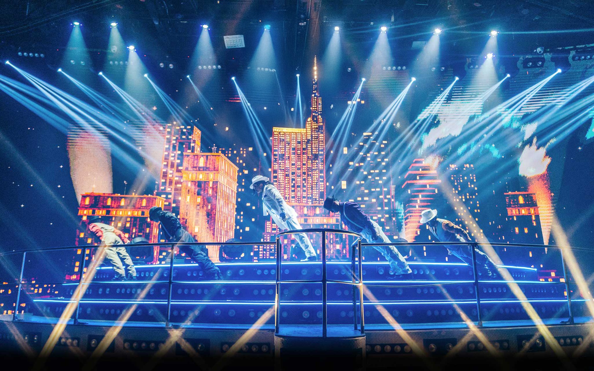 Performers on stage at Coco Bongo Disco with cityscape backdrop and vibrant lights.