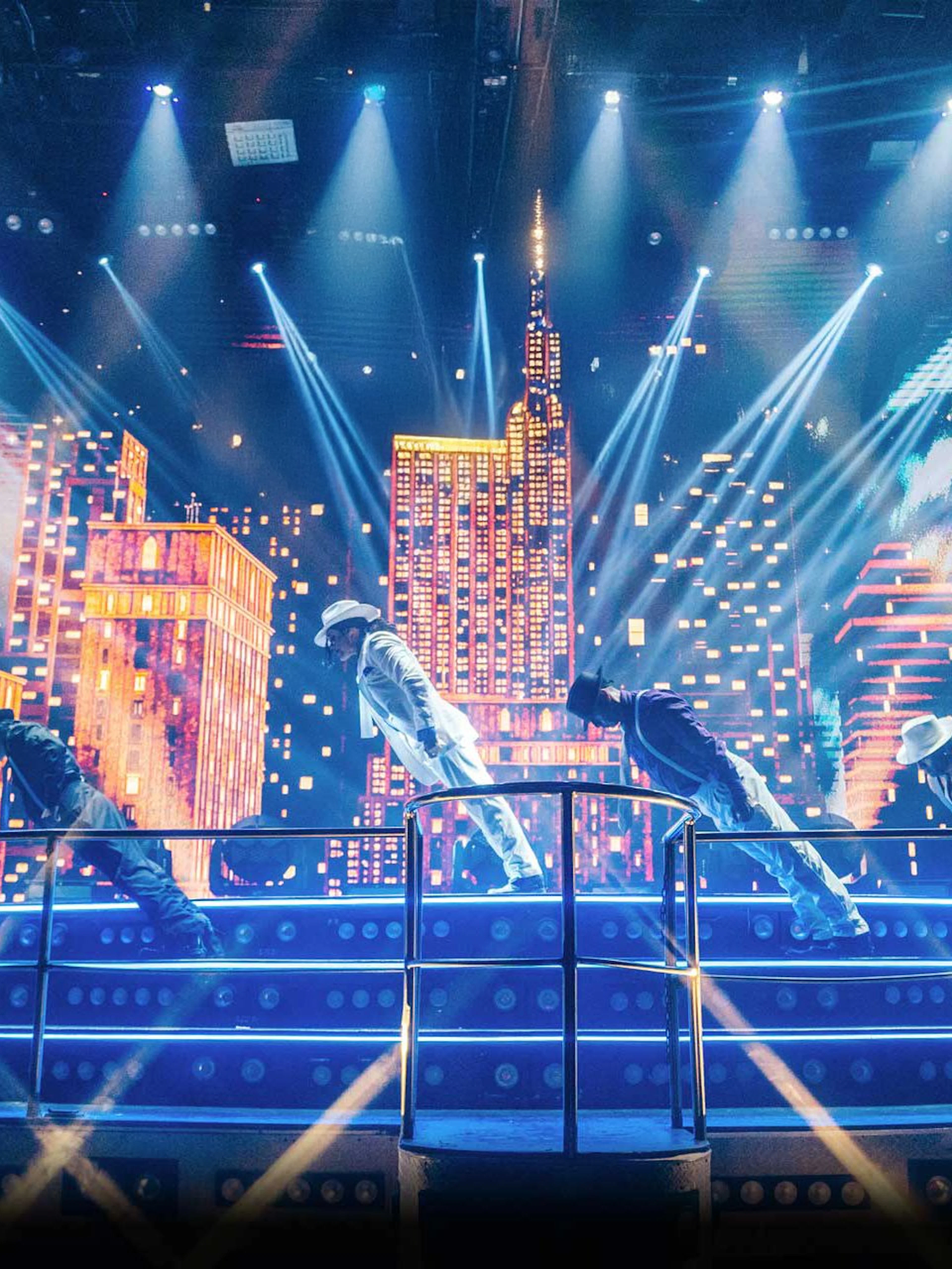 Performers on stage at Coco Bongo Disco with cityscape backdrop and vibrant lights.