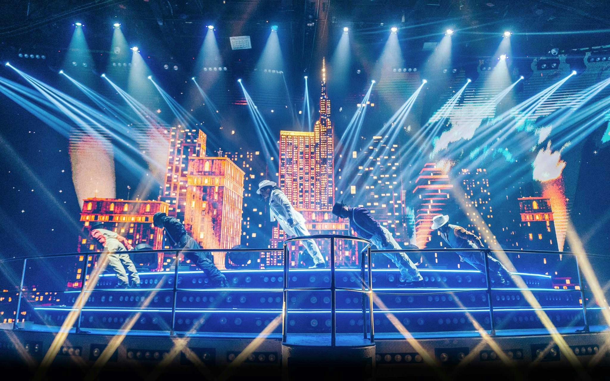 Performers on stage at Coco Bongo Disco with cityscape backdrop and vibrant lights.