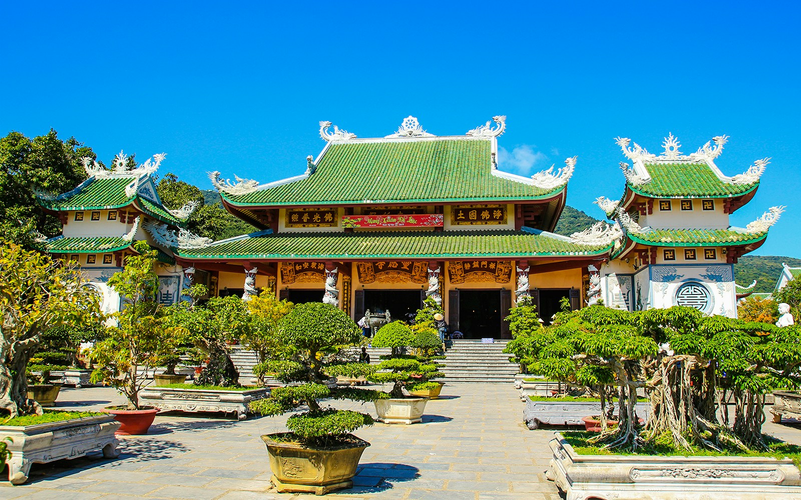 Linh Ung Pagoda entrance with green-tiled roof and bonsai trees in Da Nang, Vietnam.