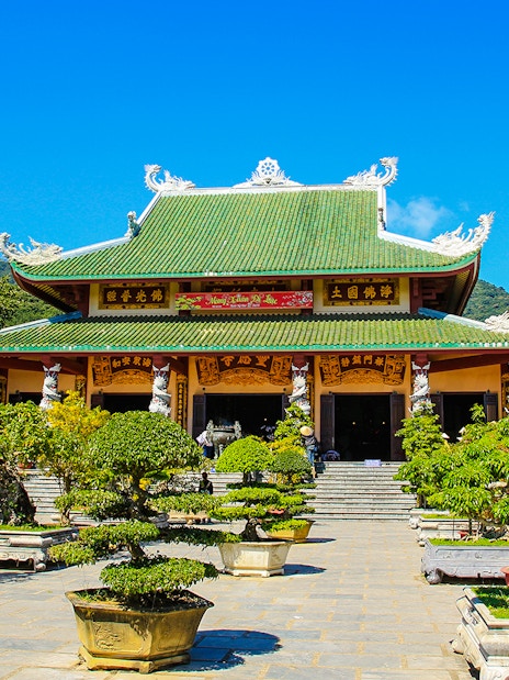 Linh Ung Pagoda entrance with green-tiled roof and bonsai trees in Da Nang, Vietnam.