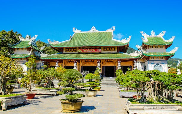 Linh Ung Pagoda entrance with green-tiled roof and bonsai trees in Da Nang, Vietnam.
