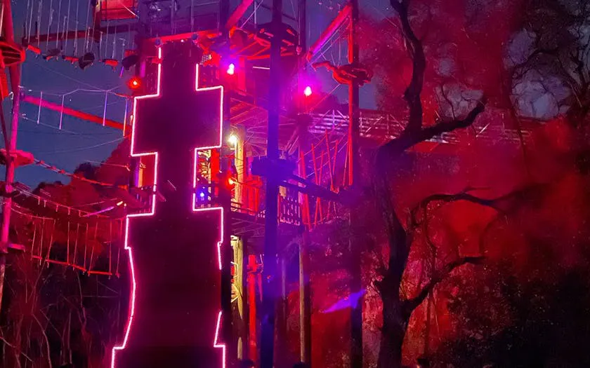 Nighttime zipline course illuminated with colorful lights in a forest setting.