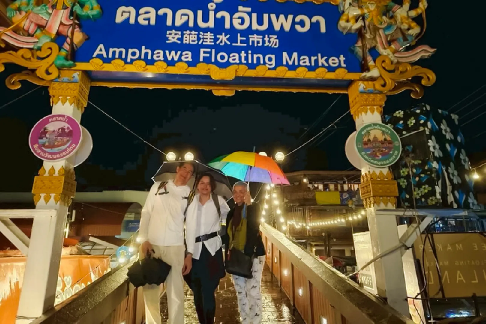 Visitors with umbrellas at Amphawa Floating Market entrance during a night tour from Laem Chabang, Pattaya.