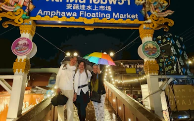 Visitors with umbrellas at Amphawa Floating Market entrance during a night tour from Laem Chabang, Pattaya.