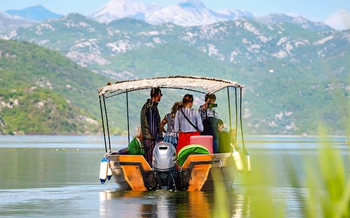 Group on a canopy boat touring Lake Skadar with mountain views.