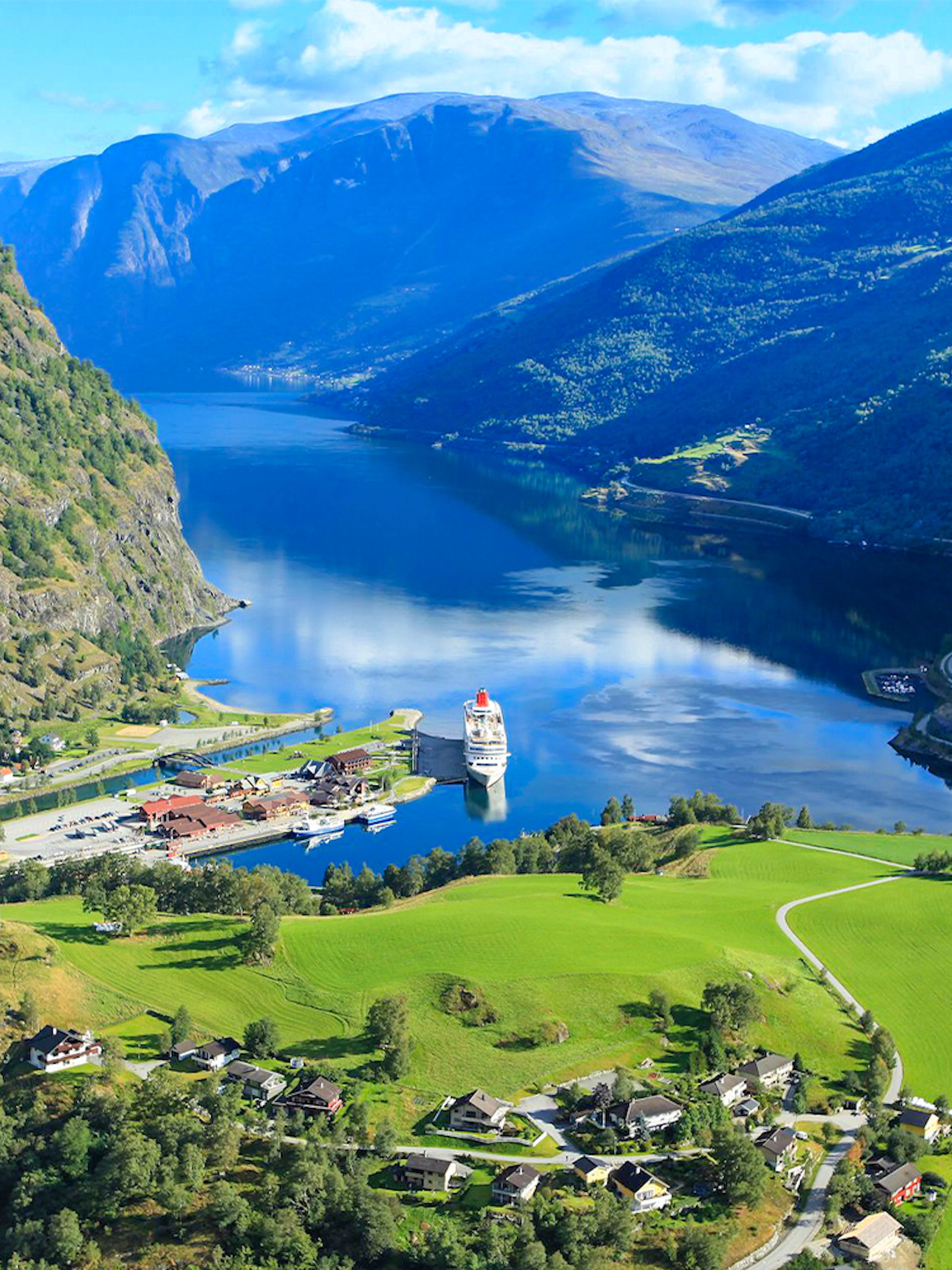 Nærøyfjord view with cruise ship docked, surrounded by mountains and green fields, part of Bergen day tour.