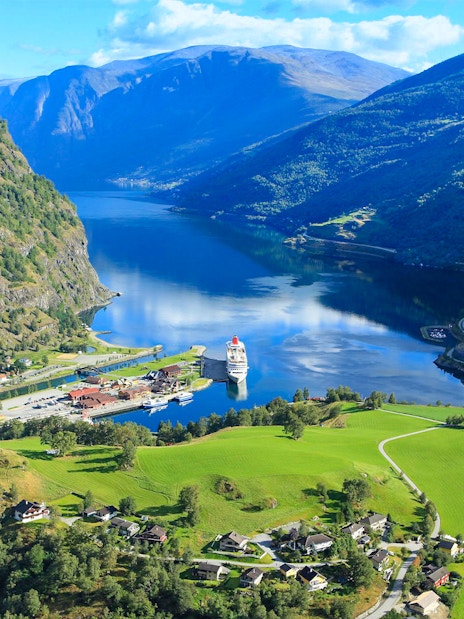 Nærøyfjord view with cruise ship docked, surrounded by mountains and green fields, part of Bergen day tour.