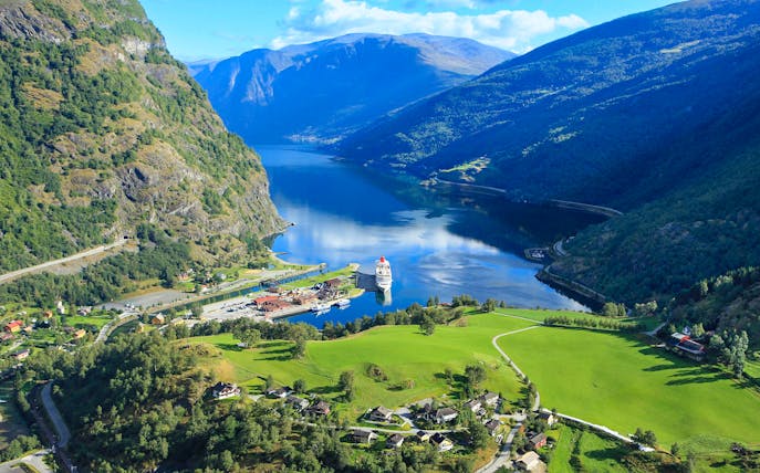 Nærøyfjord view with cruise ship docked, surrounded by mountains and green fields, part of Bergen day tour.