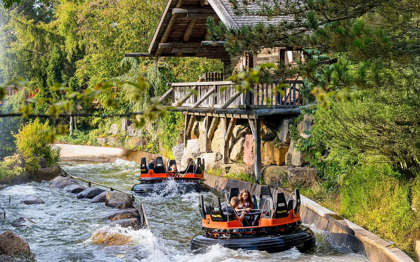 River raft ride at Heide Park Resort, Hamburg, with people navigating rapids near a wooden cabin.
