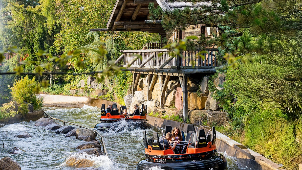 River raft ride at Heide Park Resort, Hamburg, with people navigating rapids near a wooden cabin.