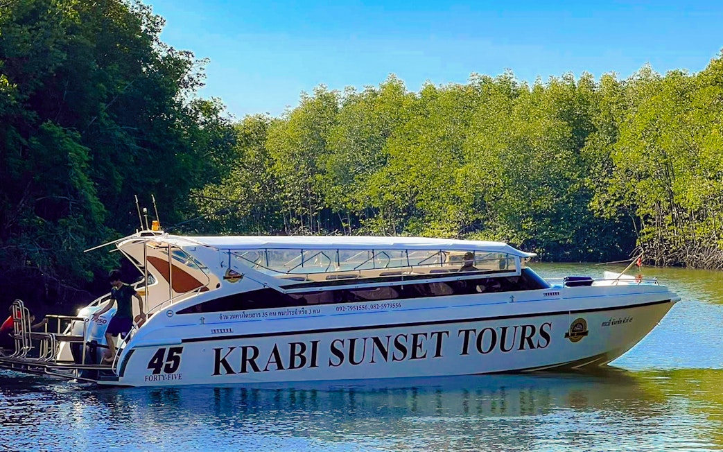 Speedboat for Krabi Sunset Tours on water near lush greenery, Phi Phi Islands.