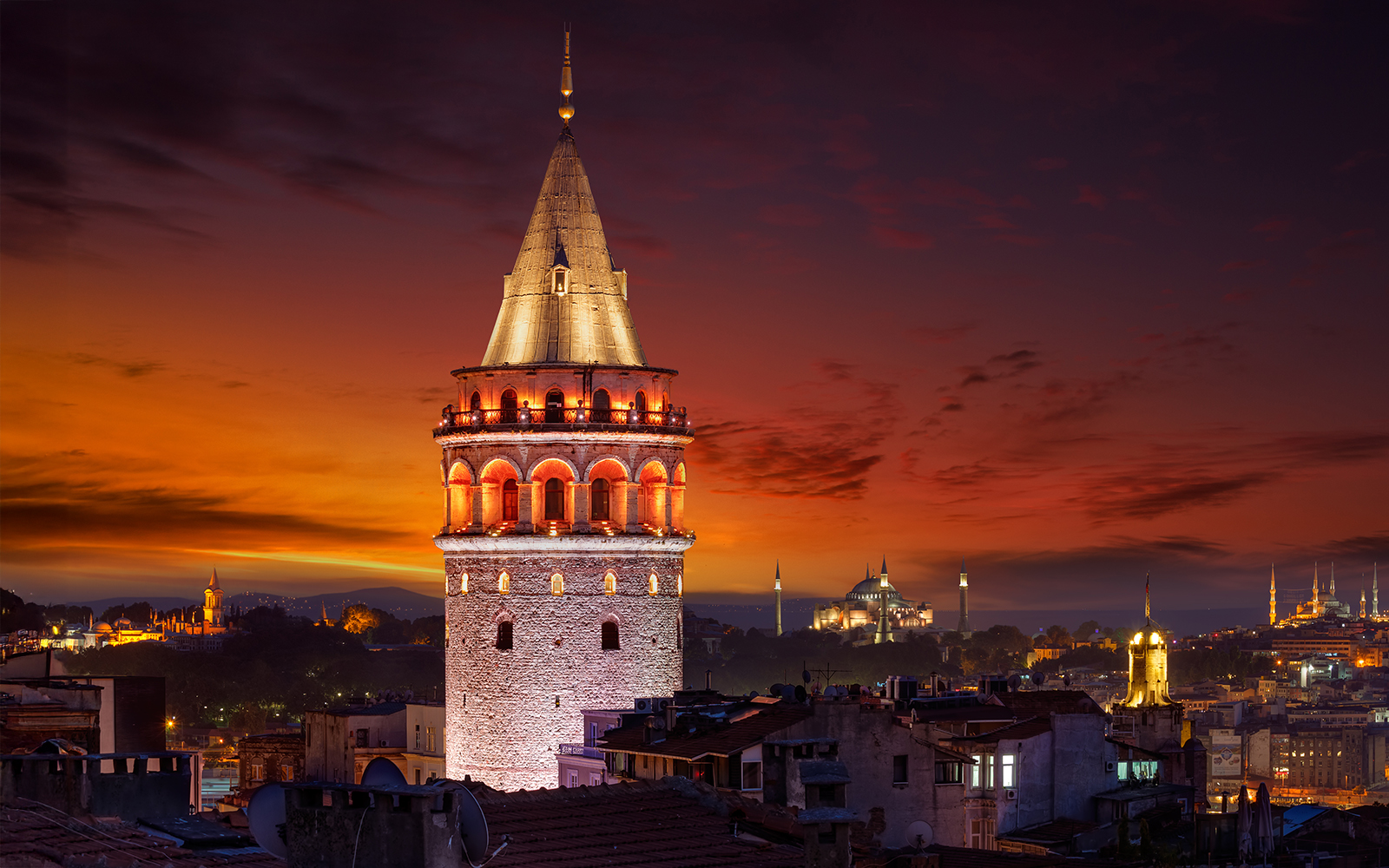 Galata Tower illuminated at night in Beyoglu, Istanbul, with a sunset sky.