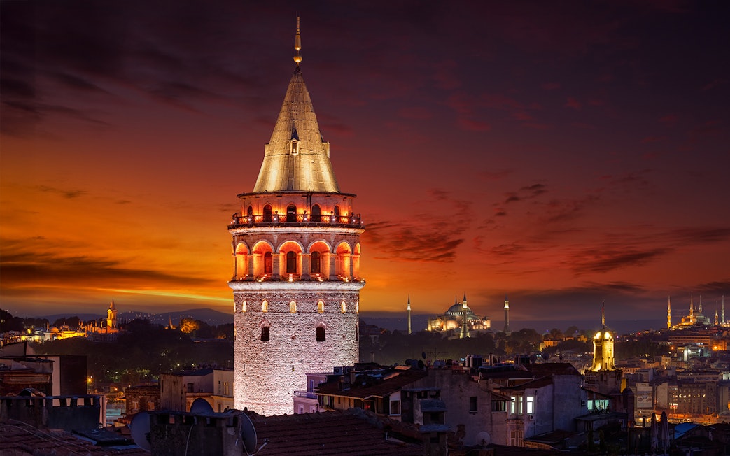 Galata Tower illuminated at night in Beyoglu, Istanbul, with a sunset sky.