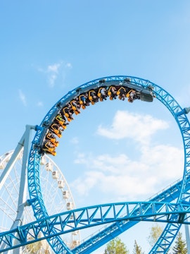 Roller coaster loop at MagicLand Theme Park with Ferris wheel in background.