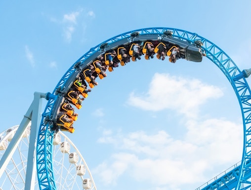 Roller coaster loop at MagicLand Theme Park with Ferris wheel in background.