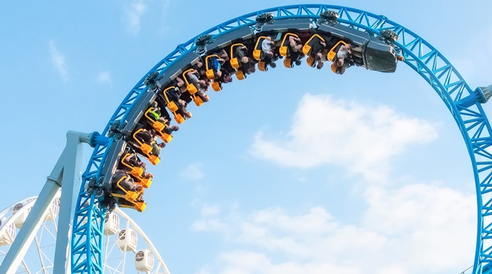 Roller coaster loop at MagicLand Theme Park with Ferris wheel in background.