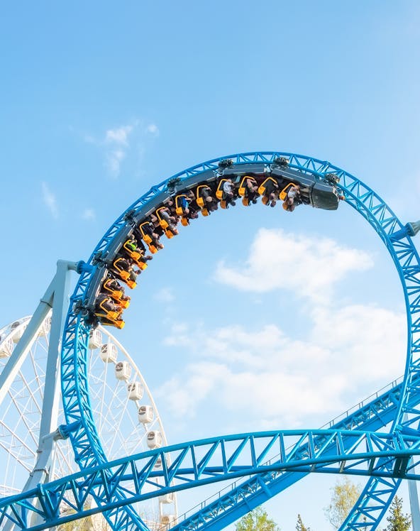 Roller coaster loop at MagicLand Theme Park with Ferris wheel in background.