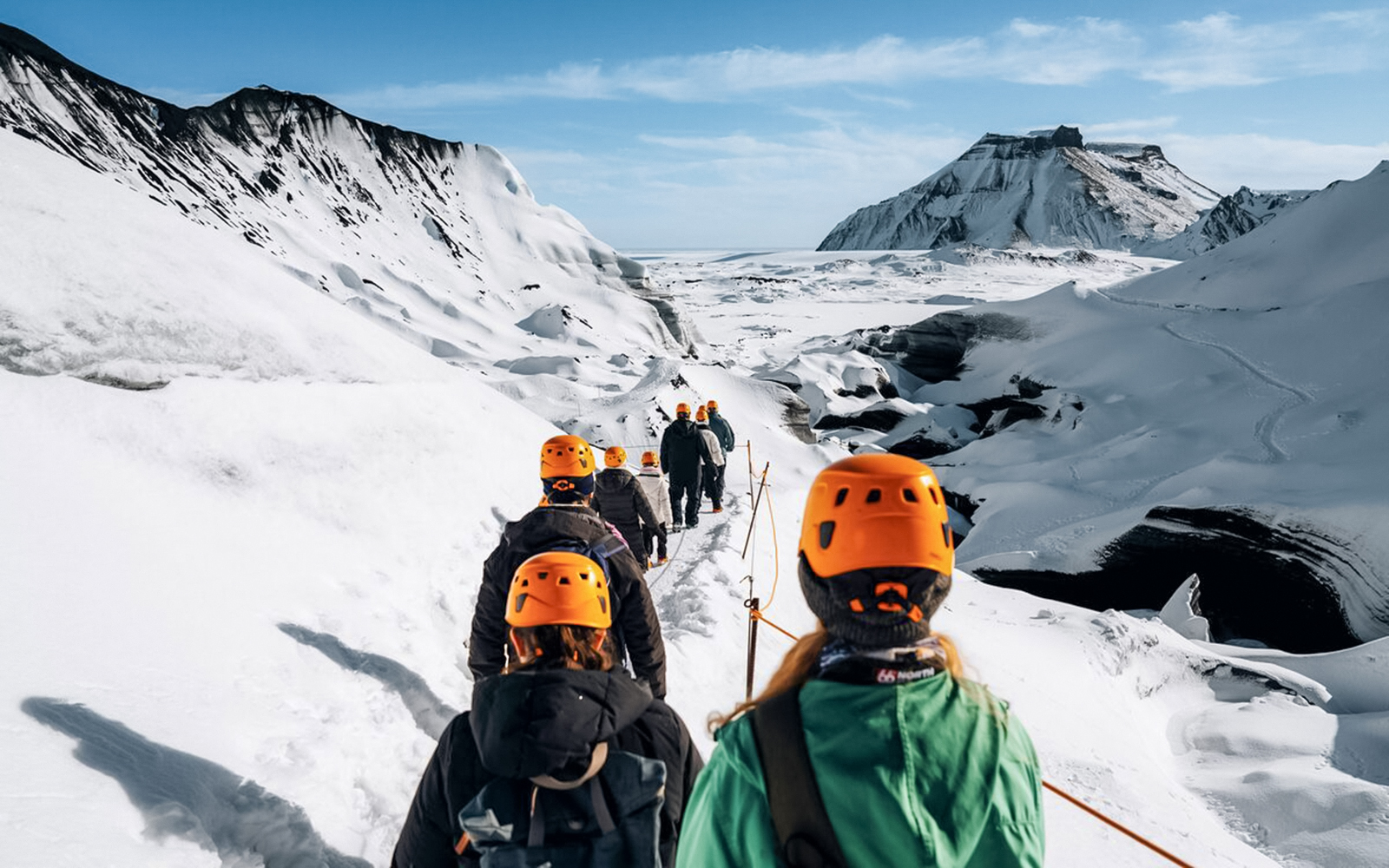 Hikers in orange helmets trekking towards Katla Ice Cave in Iceland.