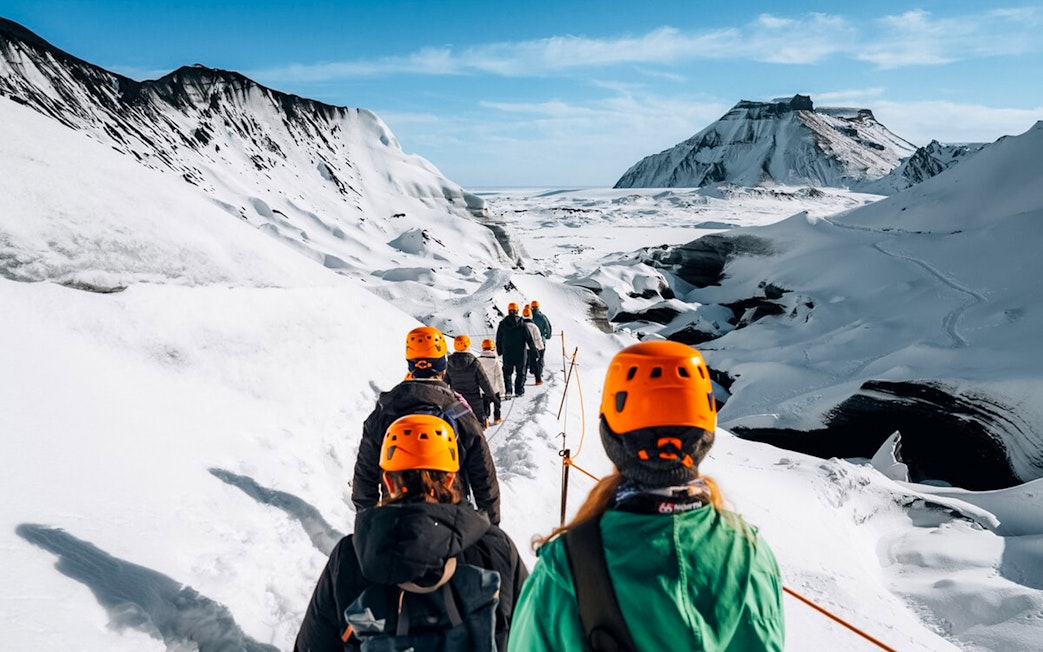 Hikers in orange helmets trekking towards Katla Ice Cave in Iceland.