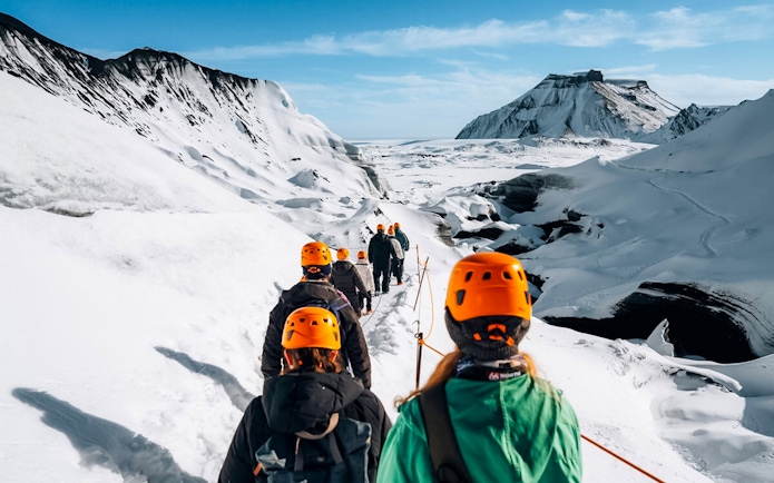 Hikers in orange helmets trekking towards Katla Ice Cave in Iceland.