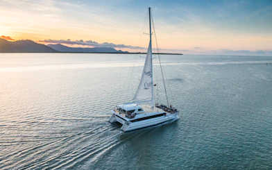 Sailboat on water at sunset with mountains in distance, Cairns, Australia.