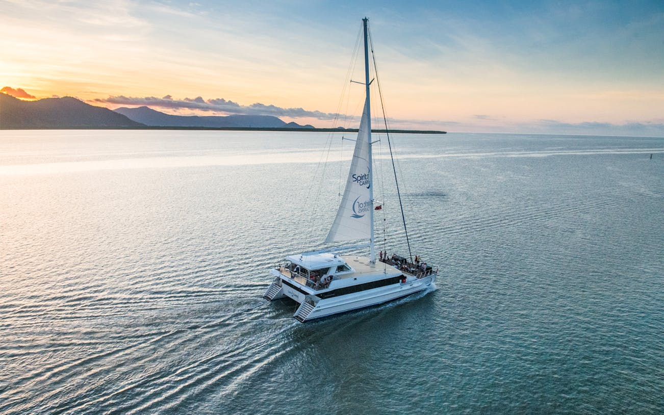 Sailboat on water at sunset with mountains in distance, Cairns, Australia.