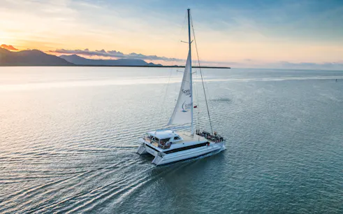 Sailboat on water at sunset with mountains in distance, Cairns, Australia.