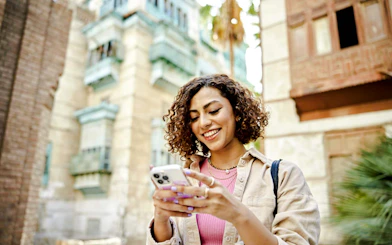 Person using smartphone in Lisbon with historic buildings in the background.