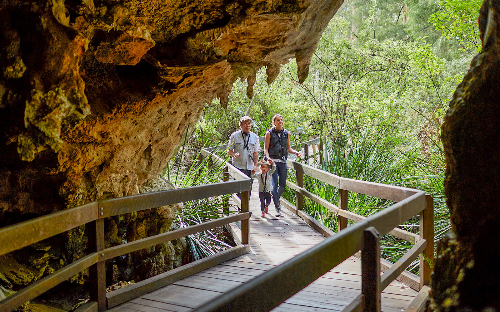 Visitors walking on a wooden path through Mammoth Cave, Margaret River, surrounded by greenery.