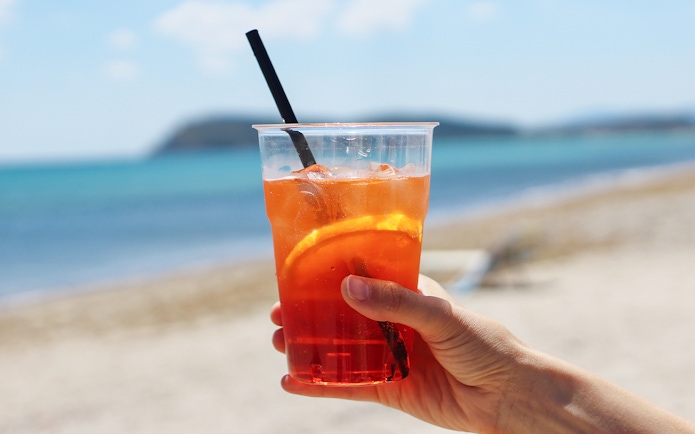 Hand holding a drink with orange slice on Cala Mariolu beach during boat tour.