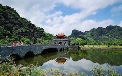 Bridge leading to Hoa Lu ancient capital in Vietnam with lush mountains and reflective water.
