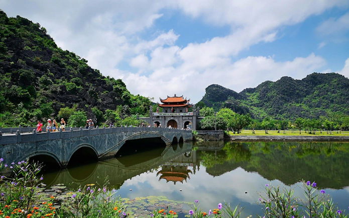 Bridge leading to Hoa Lu ancient capital in Vietnam with lush mountains and reflective water.