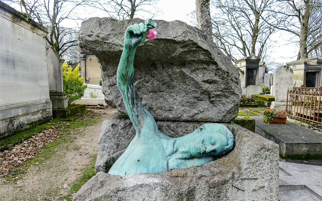 Sculpture of a figure emerging from a tomb at Père Lachaise Cemetery, Paris.