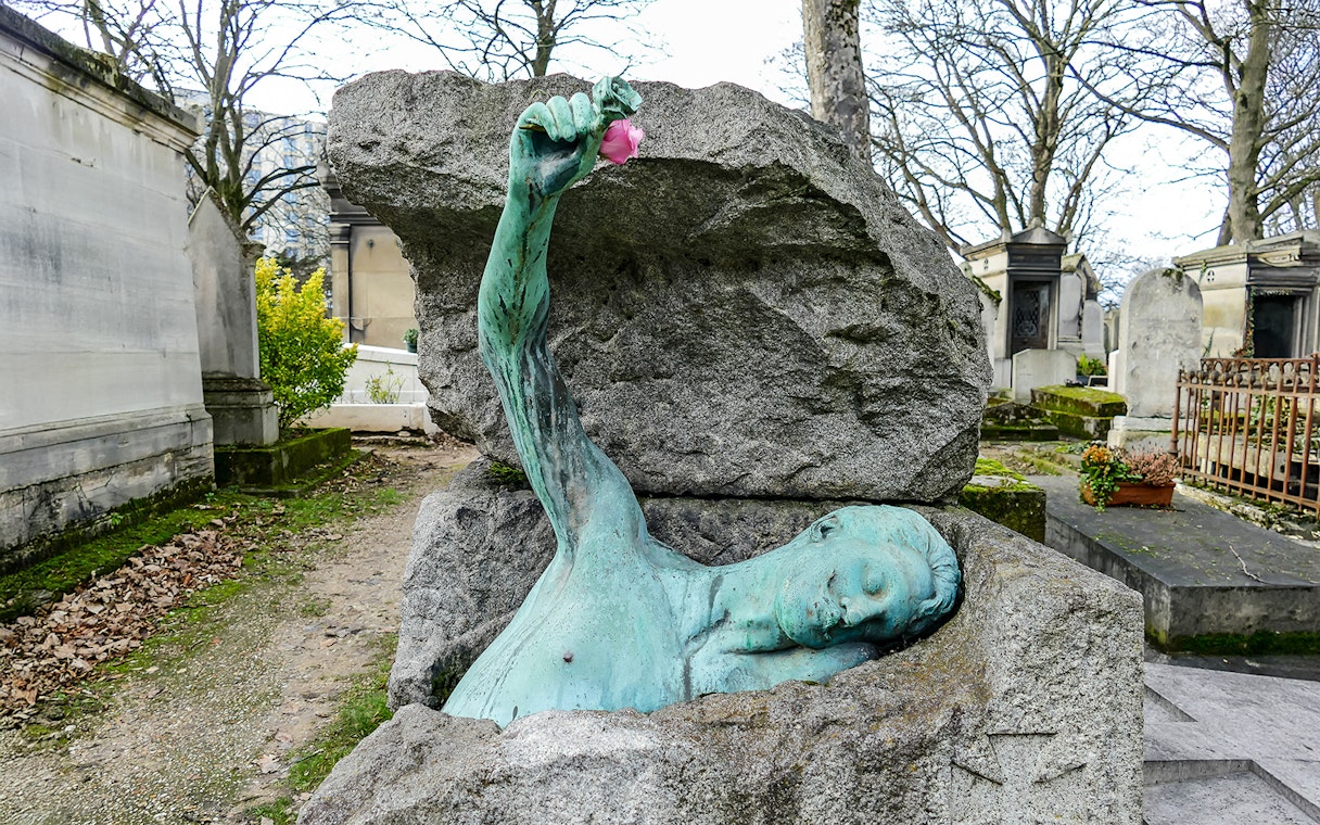 Sculpture of a figure emerging from a tomb at Père Lachaise Cemetery, Paris.