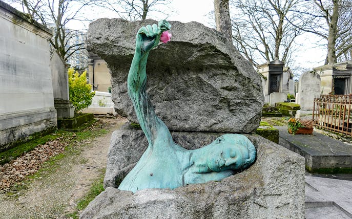 Sculpture of a figure emerging from a tomb at Père Lachaise Cemetery, Paris.